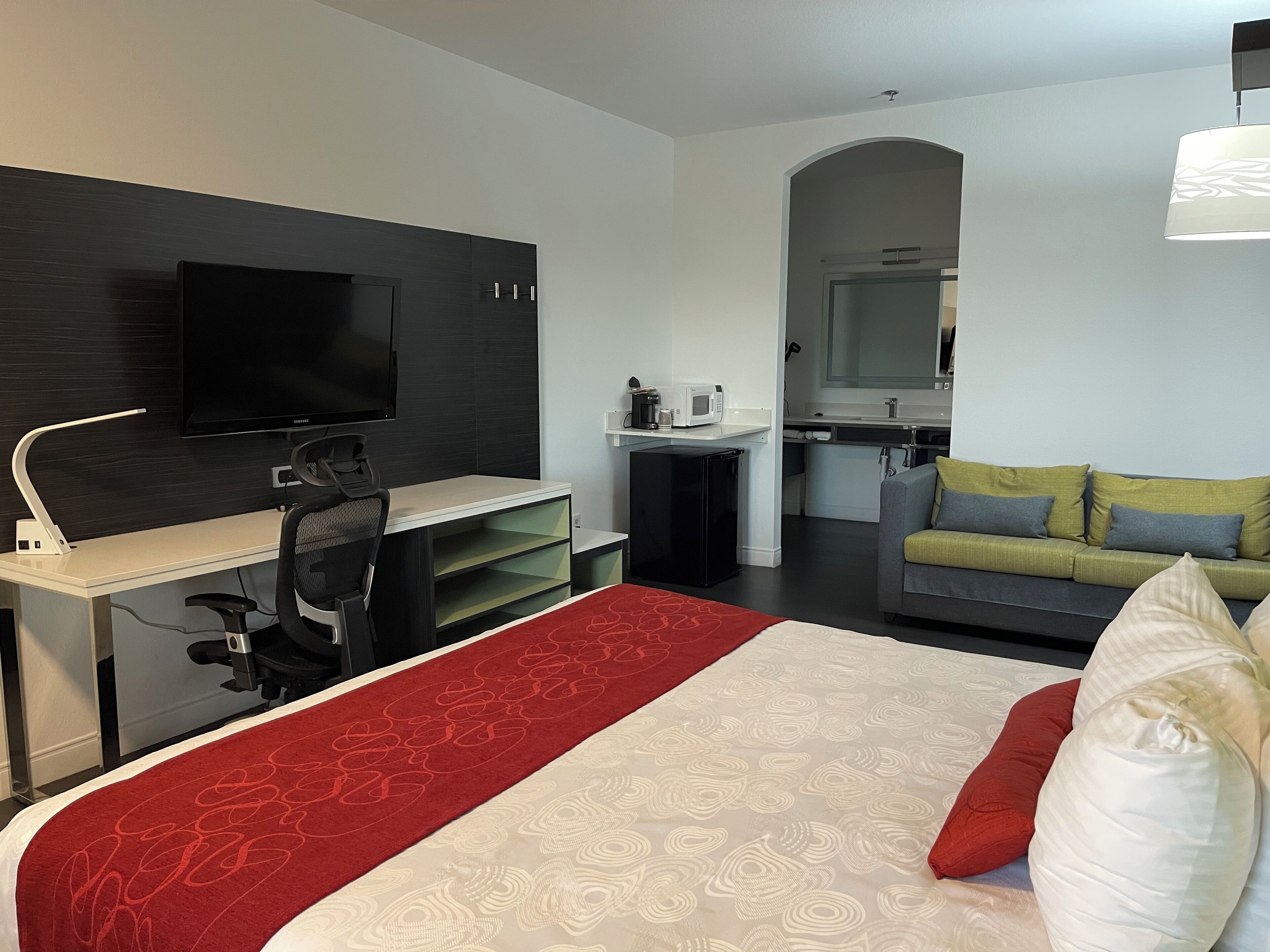 Una habitación de hotel moderna con cama, escritorio, silla, televisión, kitchenette y sofá.