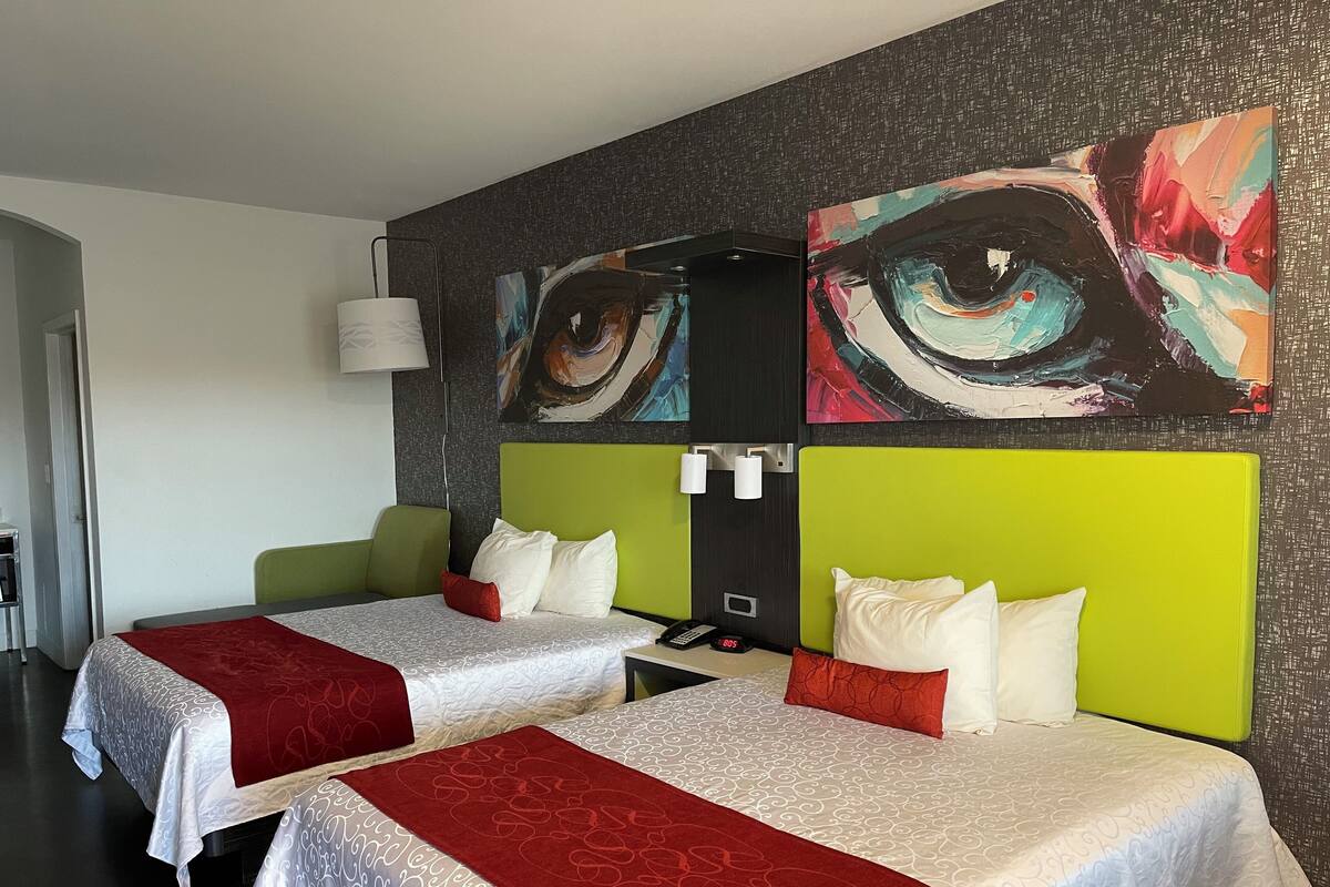 Ein Hotelzimmer mit zwei Betten, jedes mit einer rot-weißen Tagesdecke, einem grünen Kopfteil und einem an der Wand montierten Telefon.