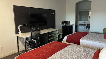 Ein Hotelzimmer mit Schreibtisch, zwei Betten, Fernseher, Mikrowelle und einer kleinen Küchenzeile.