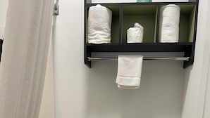 A bathroom with a toilet, a shower curtain, a towel rack with towels, and a toilet paper holder.