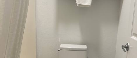 A bathroom with a toilet, a shower curtain, a towel rack with towels, and a toilet paper holder.