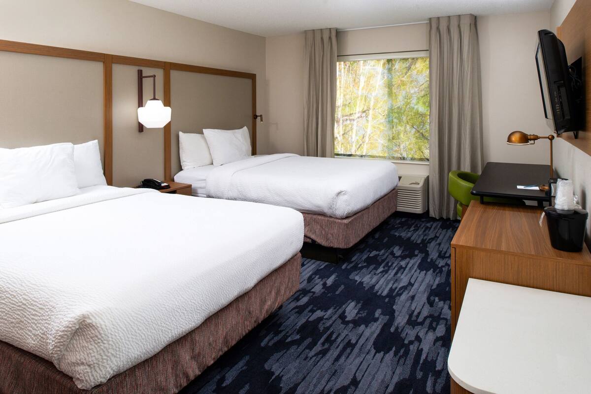 Une chambre d’hôtel avec deux lits, un bureau, une chaise, une télévision et une fenêtre avec des rideaux.