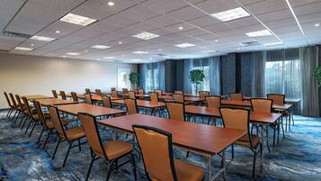 A conference room with multiple tables and chairs, large windows with curtains, and a carpeted floor.