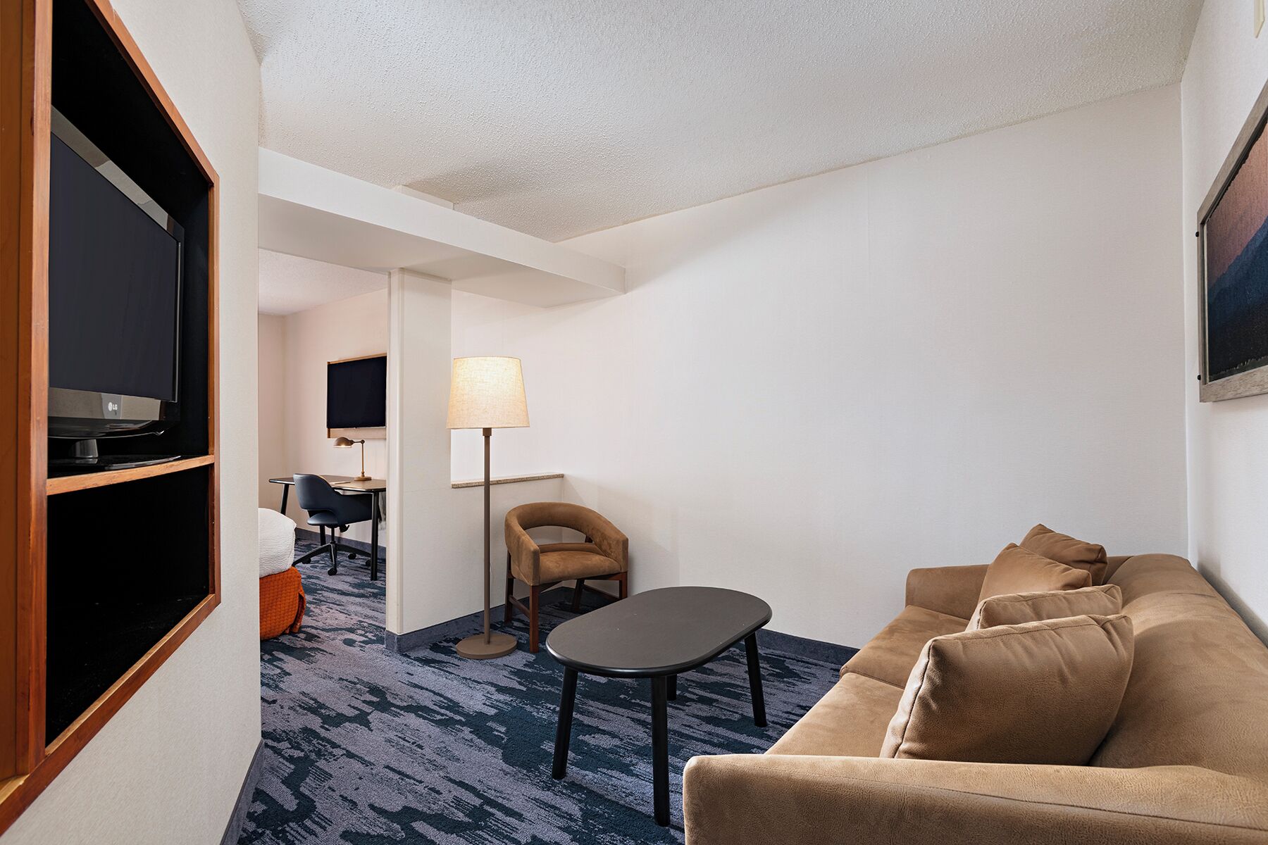 Habitación de hotel con sofá, una mesita, lámpara, televisor y escritorio con silla.