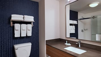 Un baño moderno con un inodoro blanco, un tocador de madera con un lavabo y un espejo grande.