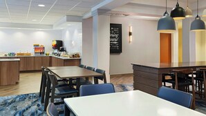 A modern hotel room with a dining area, a kitchen, and a large window.