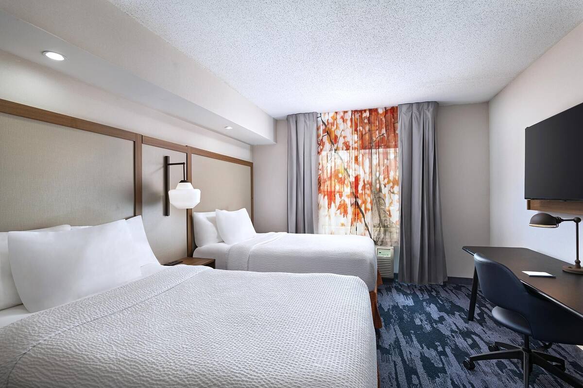 Een hotelkamer met twee bedden, een bureau, een stoel, een televisie en een raam met gordijnen.