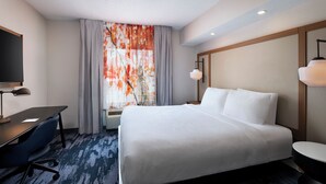 A hotel room with a bed, desk, chair, and a television.
