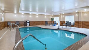 An indoor swimming pool with a tiled floor, a wooden wall, and a seating area with chairs and a table.