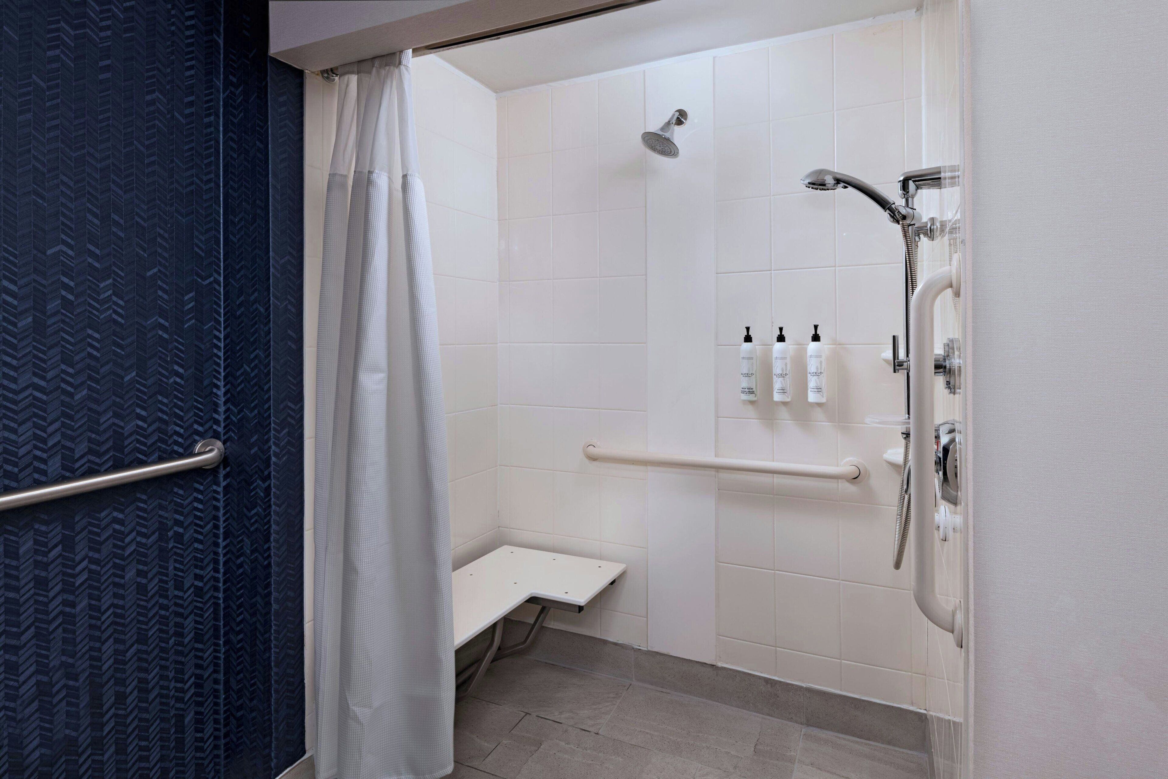 A modern bathroom with a shower, grab bars, and a bench.