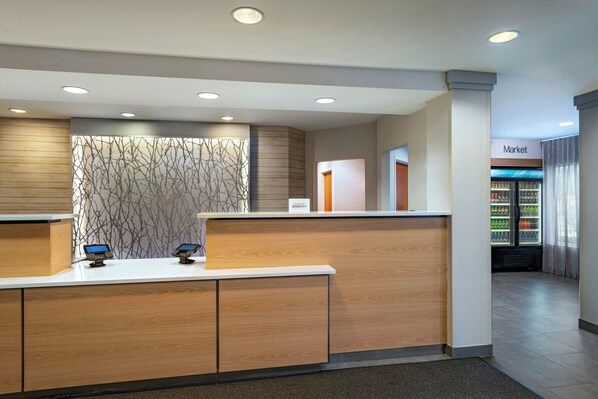 A reception desk with a modern design, a digital kiosk, and a market sign in the background. - Fairfield Inn & Suites by Marriott Edison-South Plainfield (Edison)