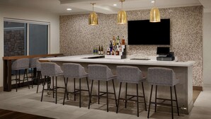 A modern kitchen with a bar area, bar stools, a countertop with bottles, and a TV mounted on the wall. - Hilton Garden Inn Las Vegas/Henderson (Henderson)