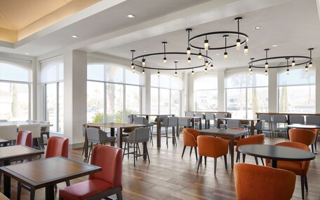 A modern dining area with high ceilings, large windows, and a variety of seating options including tables and chairs.