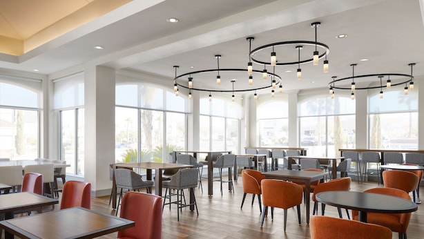 A modern dining area with high ceilings, large windows, and a variety of seating options including tables and chairs. - Hilton Garden Inn Las Vegas/Henderson (Henderson)