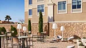 An outdoor patio with tables and chairs, a stone wall, and a building in the background. - Hilton Garden Inn Las Vegas/Henderson (Henderson)