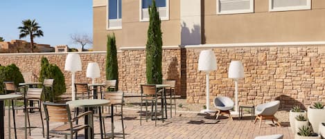 An outdoor patio with tables and chairs, a stone wall, and a building in the background.