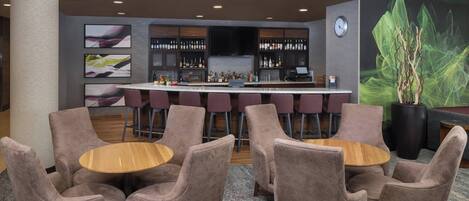 A bar area with a bar counter, multiple seating options including round tables and bar stools, and a large potted plant.