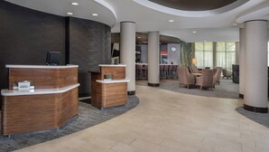 Een receptiegedeelte met een gebogen balie, een zithoek met stoelen, en een groot raam dat voor natuurlijk licht zorgt.