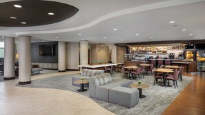 Een moderne hotellobby met een bar, zitgedeeltes en een flatscreen aan de muur.