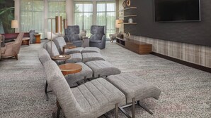 Een moderne woonkamer met een modulaire bank, fauteuils, een salontafel en een flatscreen televisie aan de muur.