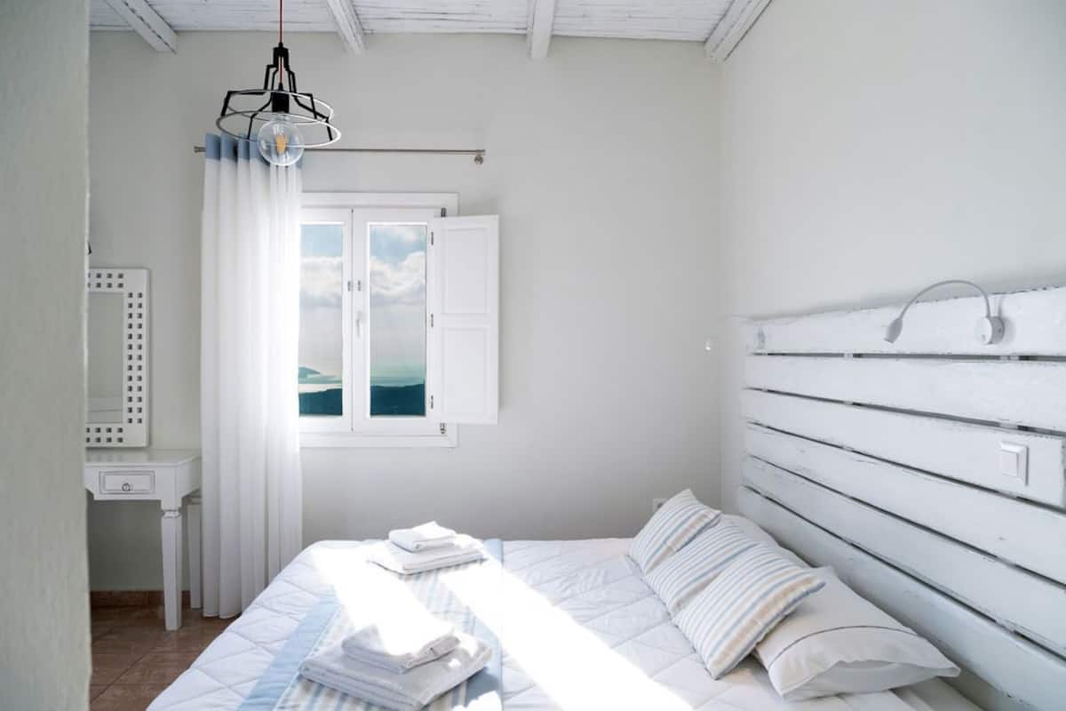 A bedroom with a bed, a bedside table, a hanging light fixture, and a window with curtains.