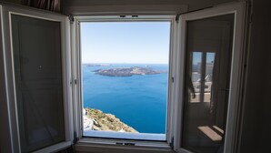 A room with a large window offering a view of the sea and distant land. - Villa Ilias Caldera Hotel (Santorini)