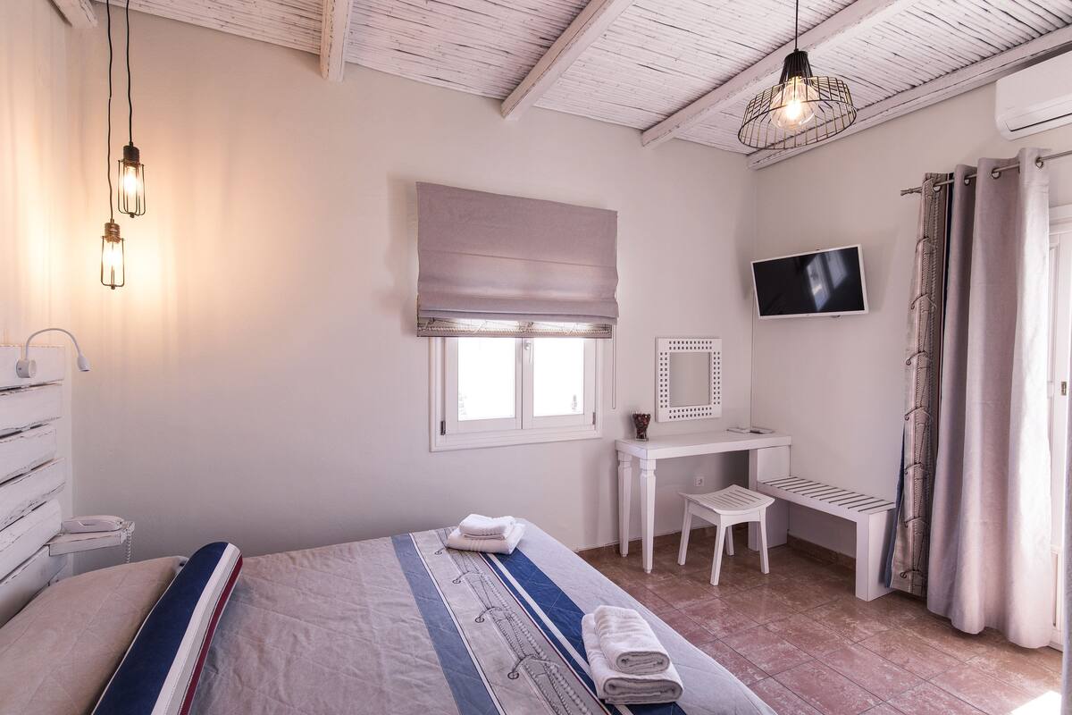 A bedroom with a bed, bedside table, vanity, and a television.