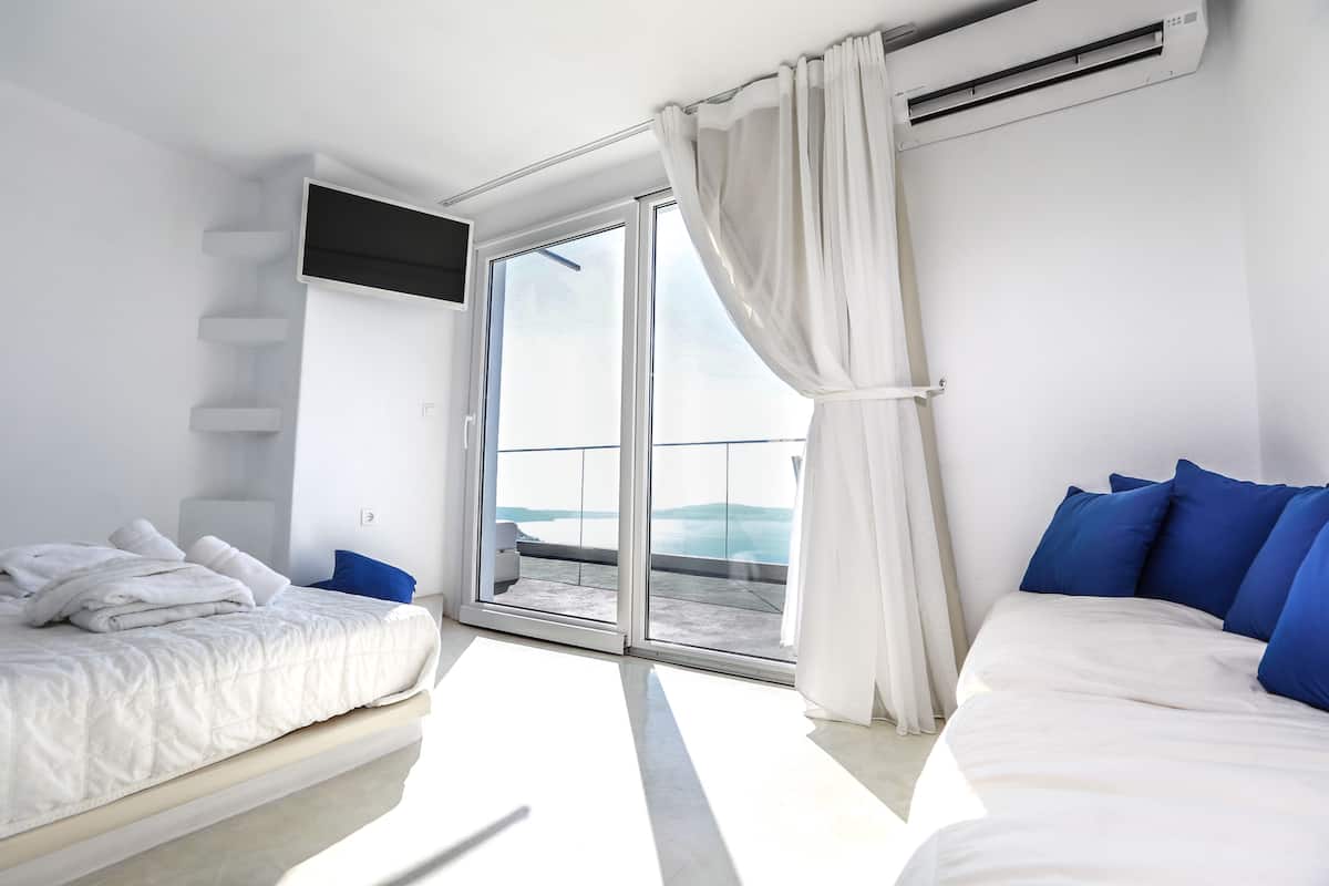A modern hotel room with a balcony, a flat-screen TV, and a bed with blue pillows.