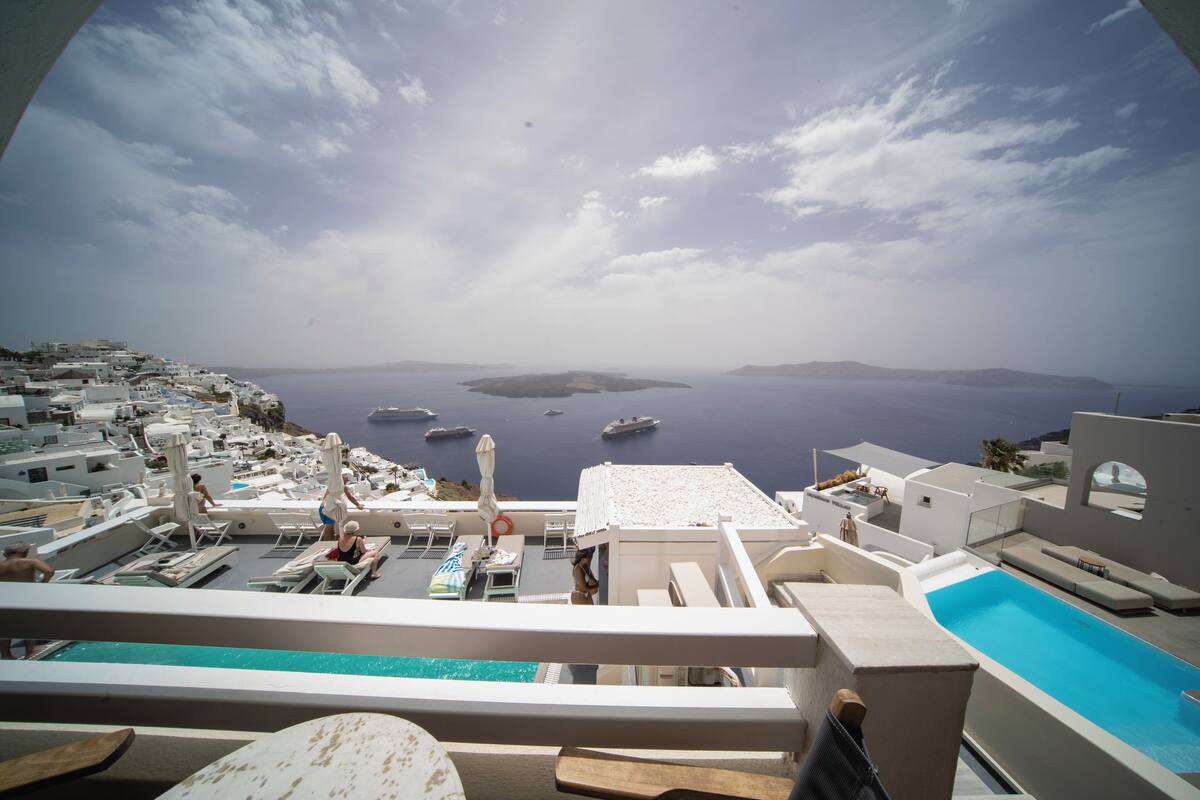 A rooftop pool area with lounge chairs and umbrellas, overlooking a coastal view with boats and islands.