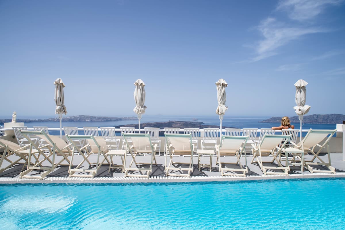 A poolside area with lounge chairs and umbrellas, overlooking a clear blue sky and distant land.