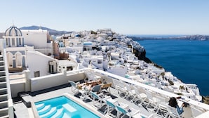 A rooftop pool area with white lounge chairs and a swimming pool, overlooking a coastal town with white buildings and a clear blue sea. - Villa Ilias Caldera Hotel (Santorini)