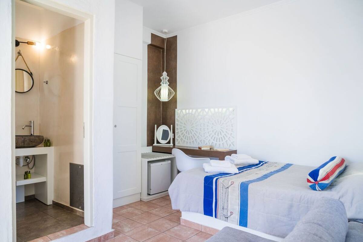 A hotel room with a bed, bedside table, and a bathroom with a sink and mirror.