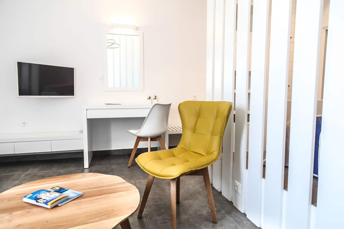 A modern room with a wooden table, a yellow chair, a white desk, a flat-screen TV, and a mirror.