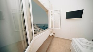 A hotel room with a large window offering a view of the sea and rocky coastline. - Villa Ilias Caldera Hotel (Santorini)