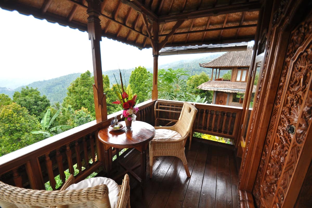 A wooden deck with wicker furniture, a table with a vase of flowers, and a view of a mountain landscape.