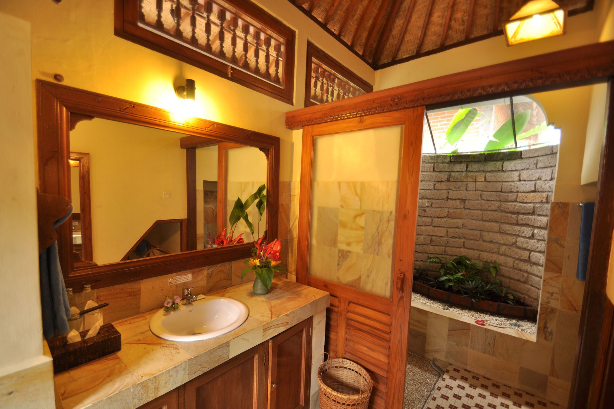 A bathroom with a wooden vanity, a large mirror, and a small window with plants.