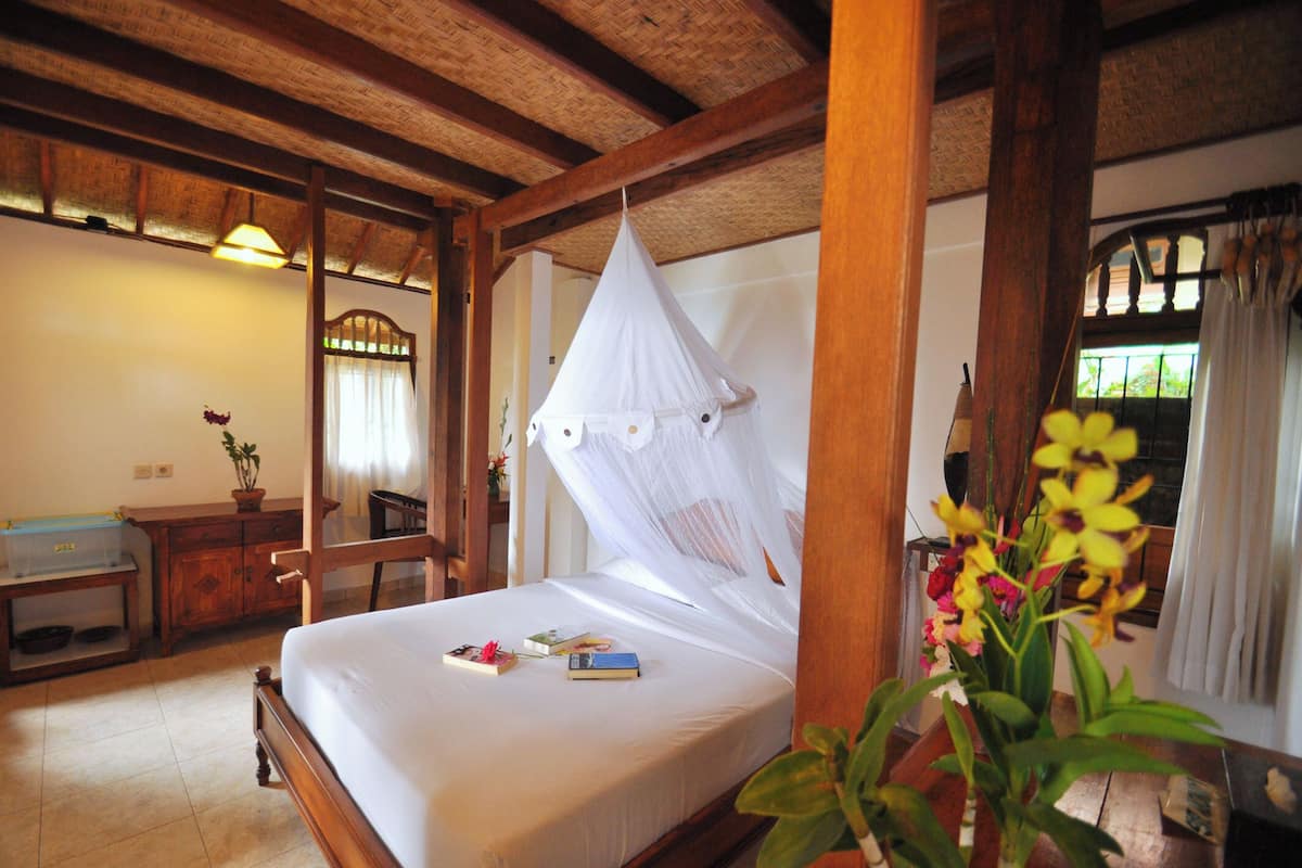 A room with a bed, wooden furniture, a mirror, and a window with curtains.