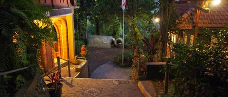 A pathway leading to a building with a traditional architectural style, surrounded by lush greenery and a flagpole.