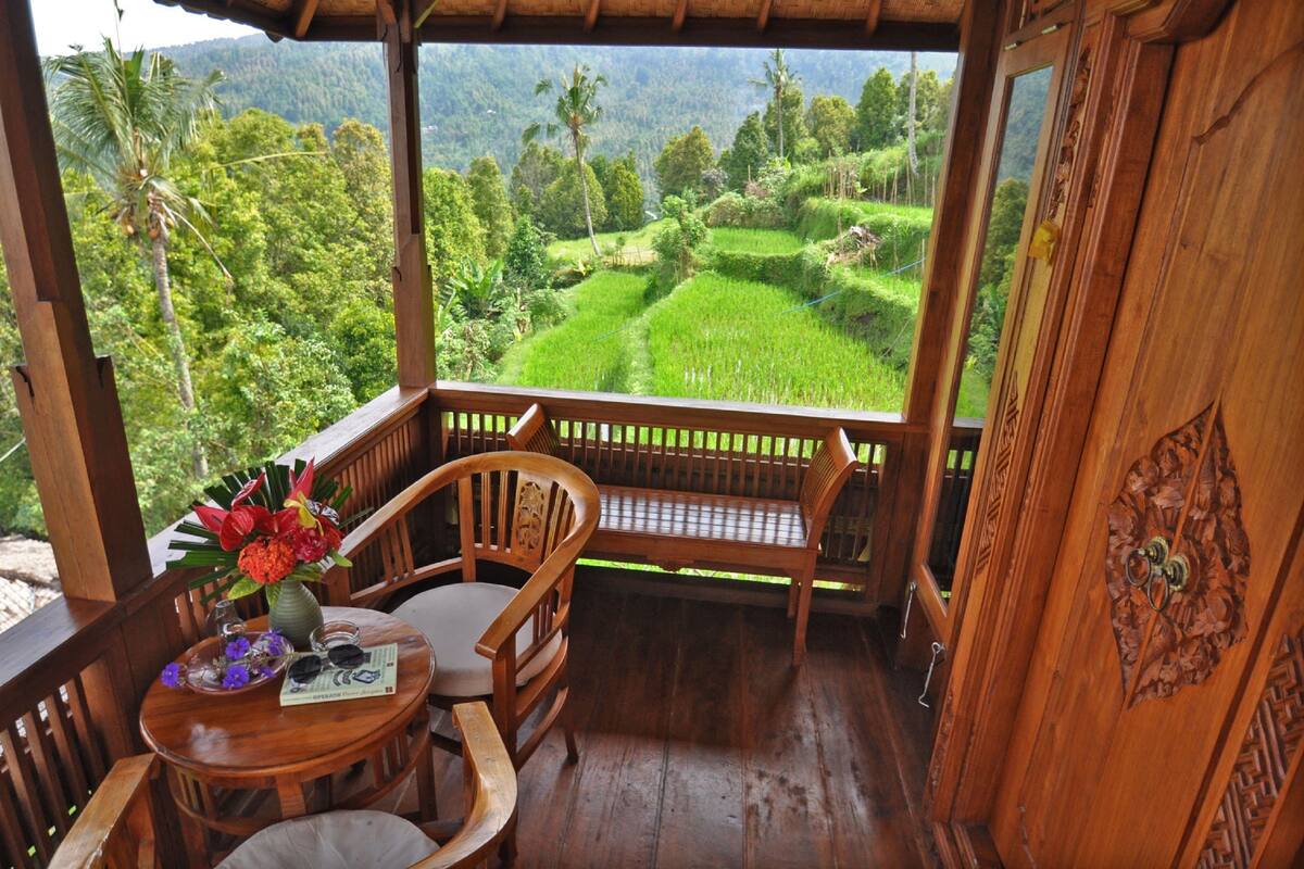 A wooden deck with a bench and table, overlooking lush green rice terraces.