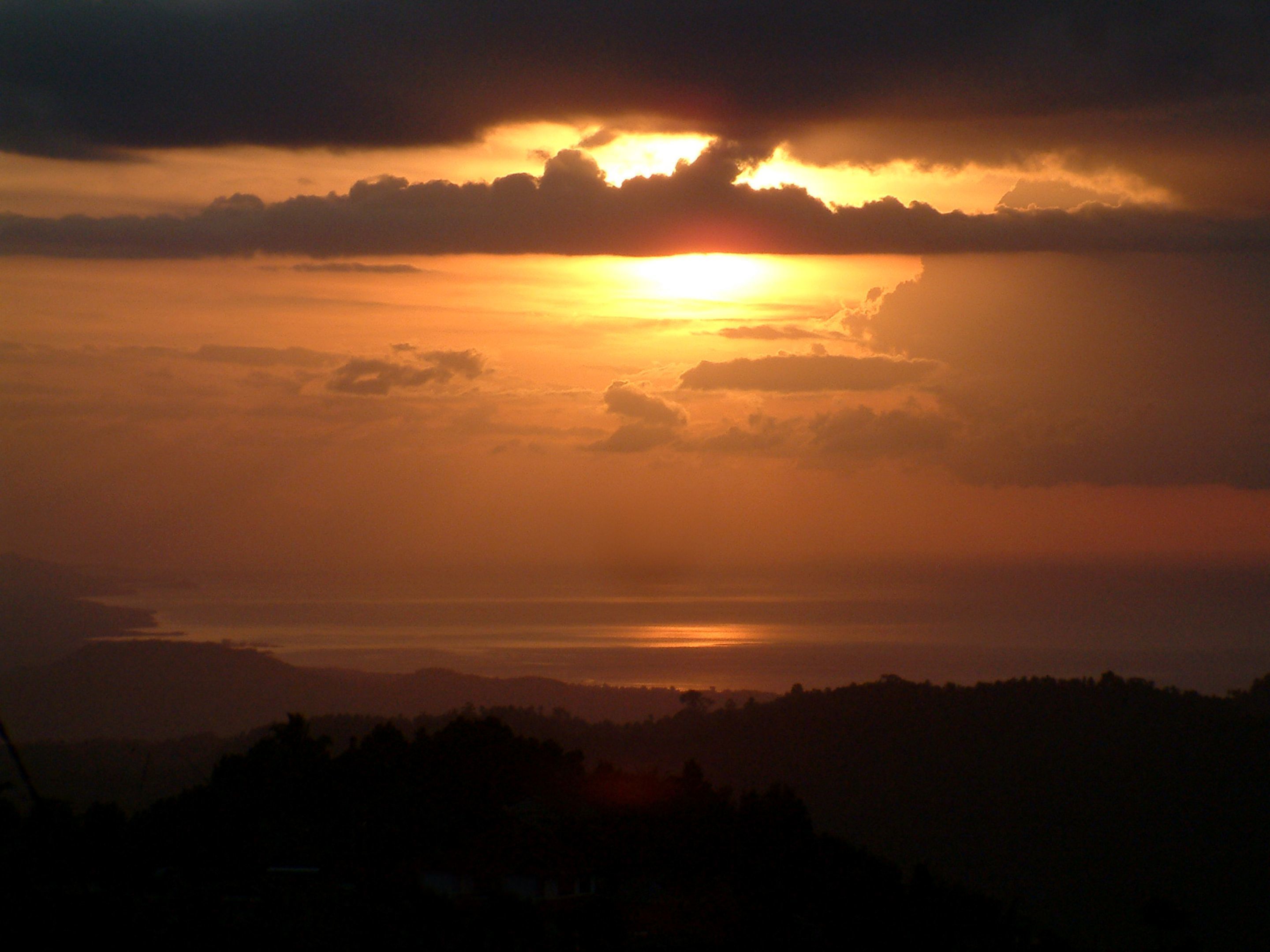 A sunset over a body of water with a silhouette of hills in the foreground.