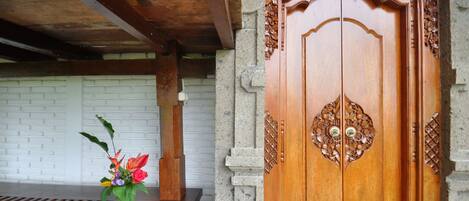 A wooden door with intricate carvings, a white brick wall, and a wooden bench with a flower vase.