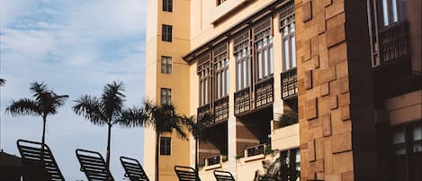 A high-rise building with multiple balconies, palm trees, and sun loungers.