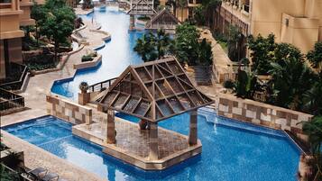 A large indoor swimming pool with a central pavilion, surrounded by high-rise buildings and lush greenery.