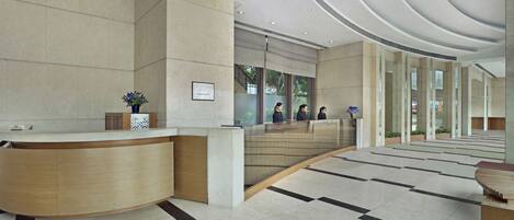 A modern reception area with a curved reception desk, a large mirror, and a check-in counter.
