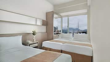 A hotel room with two beds, a bedside table with a phone, a mirror, and a large window with a city view.