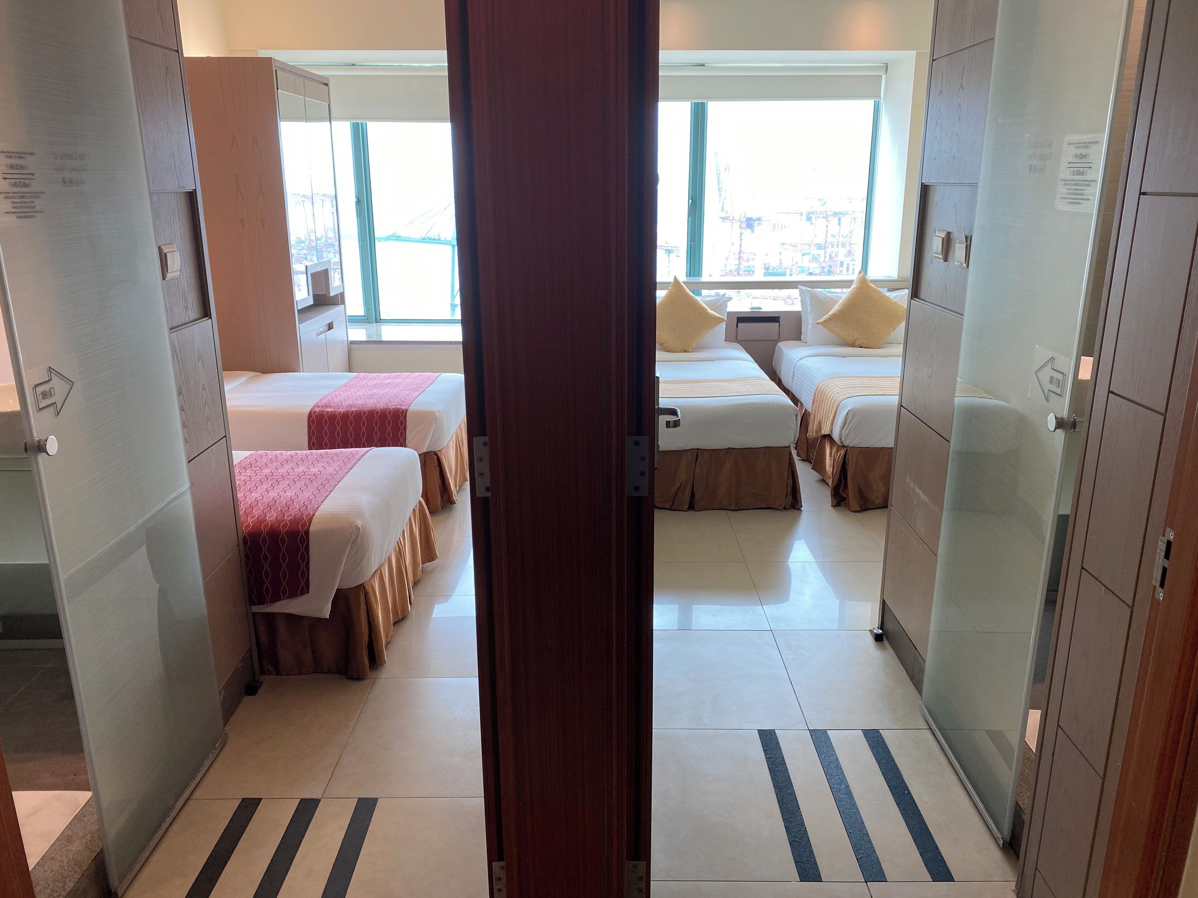 A hotel room with two beds, a small table, and a window with a view of buildings.