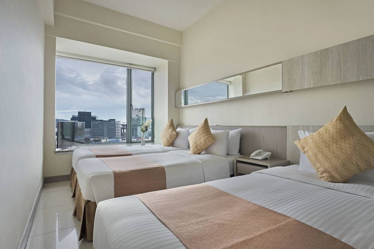 Quarto de hotel com duas camas, uma janela grande com vista para a cidade, uma mesa de cabeceira com telefone e um espelho na parede.