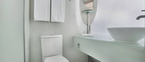 A modern bathroom with a white toilet, a glass sink, and a mirror above the sink.