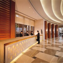 Zona de recepción de hotel con diseño moderno, que incluye un mostrador de recepción, un área de espera y un mostrador de registro.