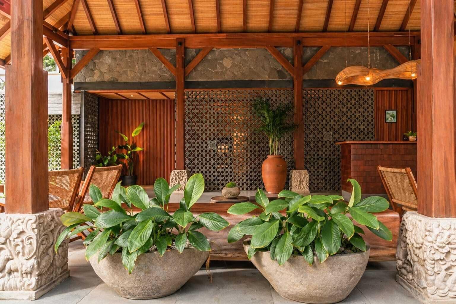 A covered outdoor seating area with stone planters, wooden furniture, and a decorative wall.
